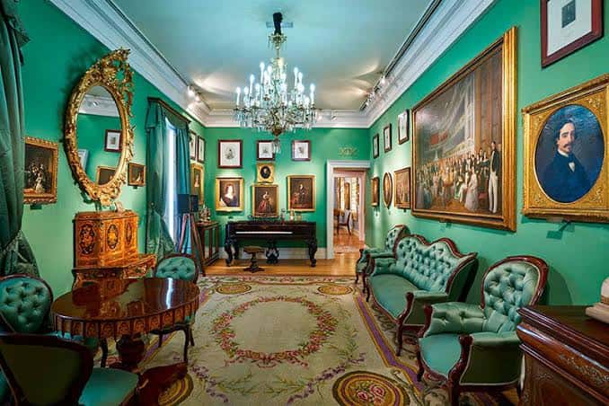 Salón principal con decoración verde, espejo dorado y piano