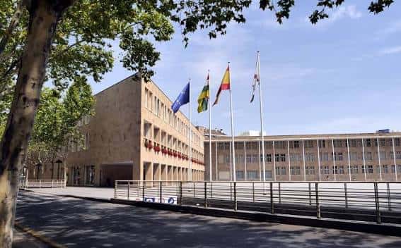 Vista lateral del Ayuntamiento de Logroño con árboles y banderas en primer plano