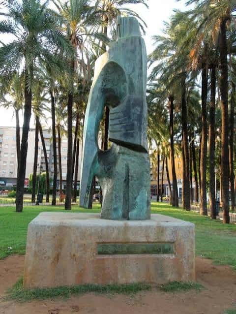 Escultura abstracta en el centro de la plaza rodeada de palmeras