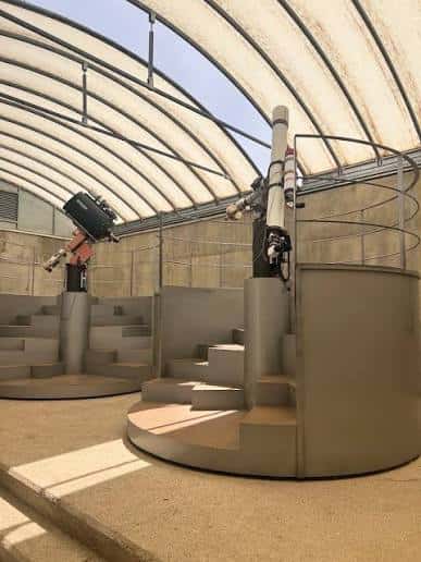 Observatorio exterior con telescopios bajo una estructura de techo curvo translúcido