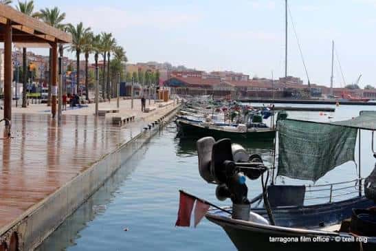 Pasarela de madera junto al puerto con palmeras y barcos atracados