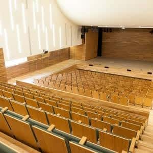 Interior del auditorio con asientos de madera y escenario iluminado