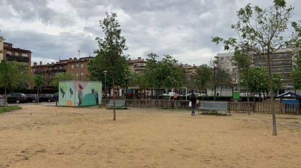 Plaza con área de juegos infantiles y árboles bajo cielo nublado