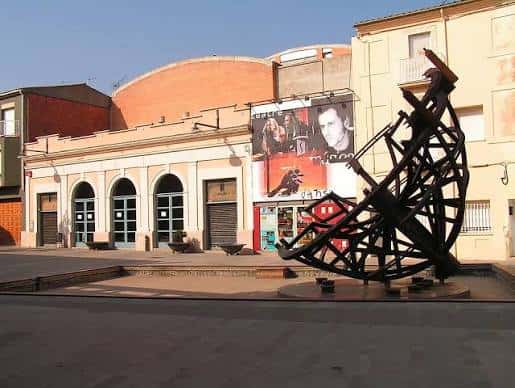 Plaza con escultura metálica y fachada de edificio con arcos