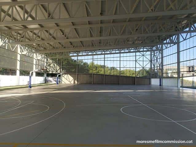 Vista interior del pabellón deportivo con canchas de baloncesto y estructura metálica