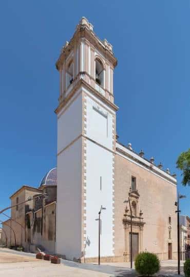 Vista exterior de la Iglesia de Nuestra Señora de la Asunción con su torre campanario bajo un cielo azul