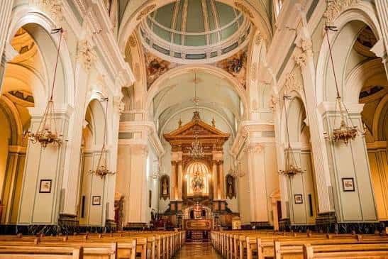 Interior de la iglesia mostrando la nave central, bóvedas y el altar mayor iluminado