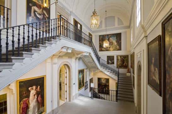 Escalera principal interior con obras de arte enmarcadas y barandilla de hierro forjado