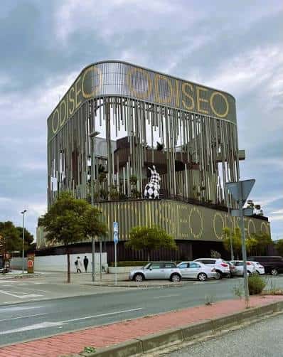 Vista exterior del centro de ocio Odiseo en Murcia con su distintiva fachada de listones verticales y el nombre del edificio en letras doradas
