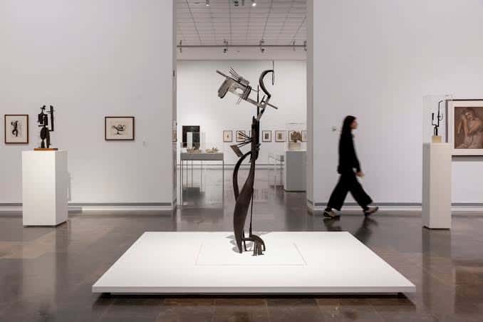 Visita a la exposición con escultura abstracta en primer plano y persona caminando