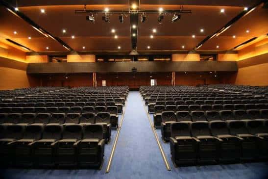 Interior del auditorio con butacas negras dispuestas en gradas y escenario iluminado