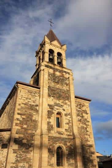 Detalle arquitectónico de la torre de la iglesia con campanas y cruz en la cúspide