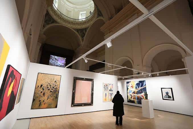 Interior del centro cultural mostrando una exposición de arte contemporáneo con obras colgadas en paredes blancas