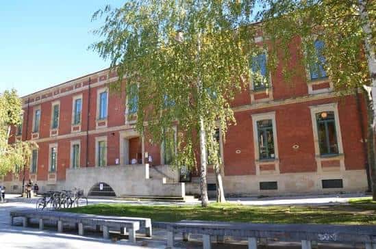 Edificio histórico del campus con fachada de ladrillo y árboles en un día soleado