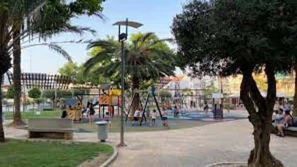 Área de juegos infantiles en el Parque de España con palmeras y personas disfrutando del espacio
