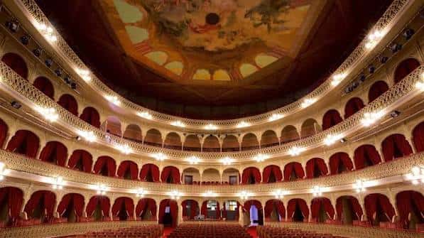 Interior del auditorio con balcones curvos, cortinas rojas y techo pintado