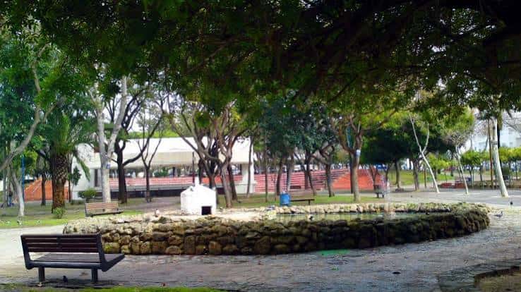 Vista del parque con fuente central y zona de descanso bajo árboles