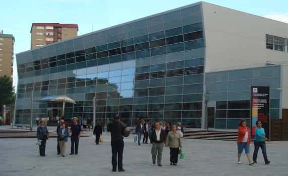 Vista exterior de la Biblioteca Bellvitge con su fachada de cristal y personas en la plaza