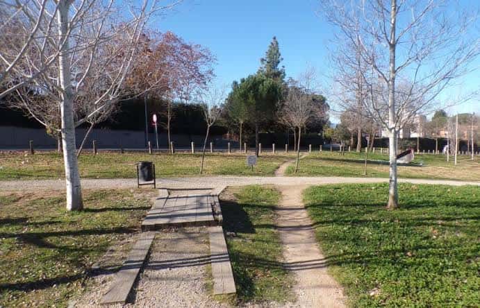 Sendero de tierra y madera que atraviesa el parque con árboles y césped