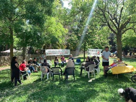 Grupo de personas reunidas en una asamblea al aire libre bajo árboles frondosos