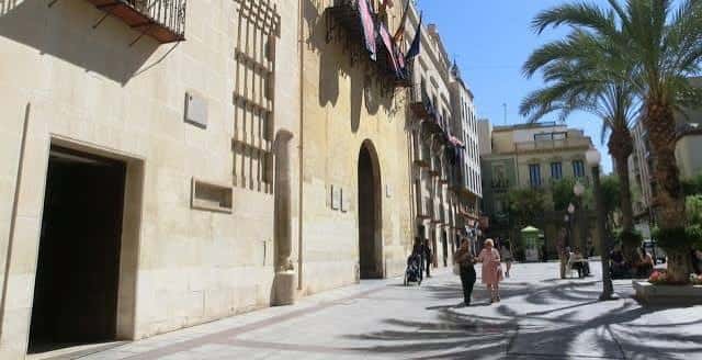 Vista exterior de la Lonja Medieval de Elche con palmeras y peatones