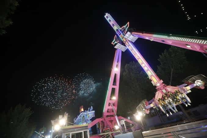 Atracción de feria iluminada con fuegos artificiales en el cielo nocturno