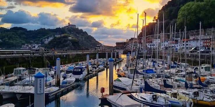 Atardecer en el puerto deportivo con veleros y el Monte Urgull iluminado