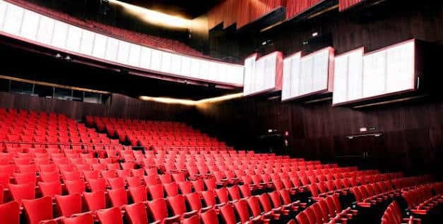 Interior del auditorio con butacas rojas dispuestas en gradas y escenario iluminado