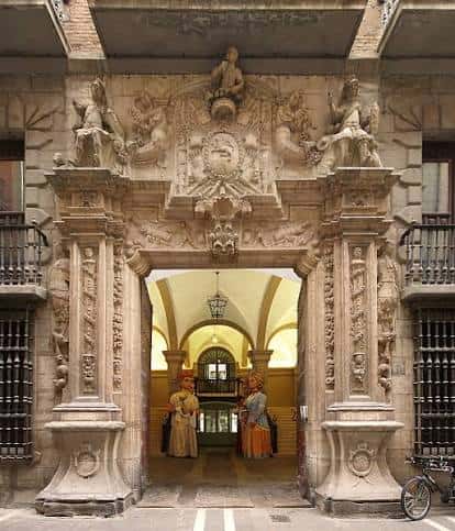 Entrada del palacio con dos figuras vestidas de época en el vestíbulo iluminado