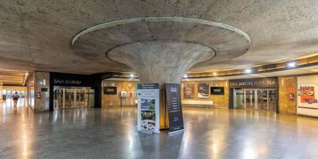 Hall principal del centro cultural con columnas de hormigón y señalización de salas