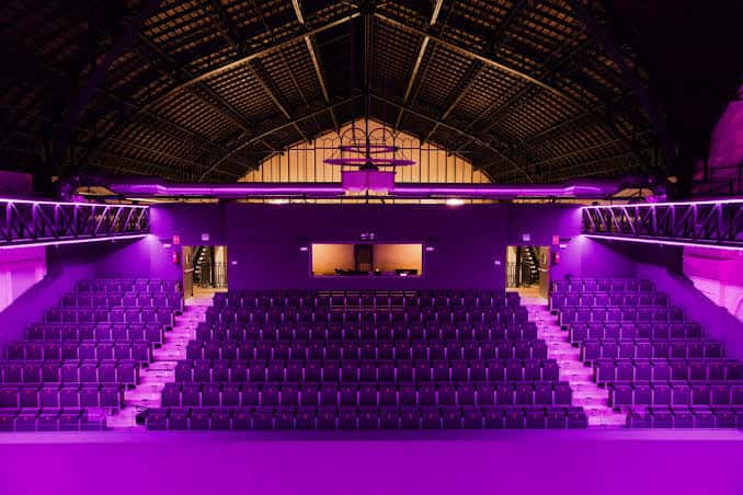 Aula magna del teatro con gradas curvas y techo de estructura metálica iluminada