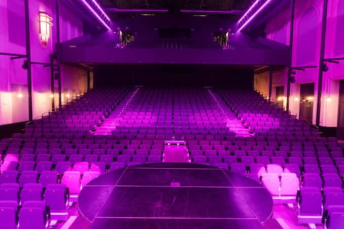 Interior del auditorio con butacas dispuestas en semicírculo y escenario central bajo luz ambiental