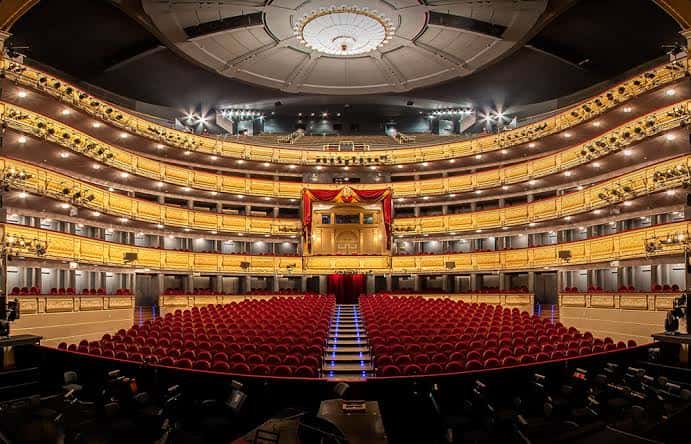 Plano general del interior del teatro con iluminación cálida y escenario central