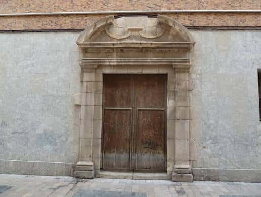 Detalle arquitectónico de una puerta de madera con marco de piedra y frontón curvo, característica del estilo histórico del edificio