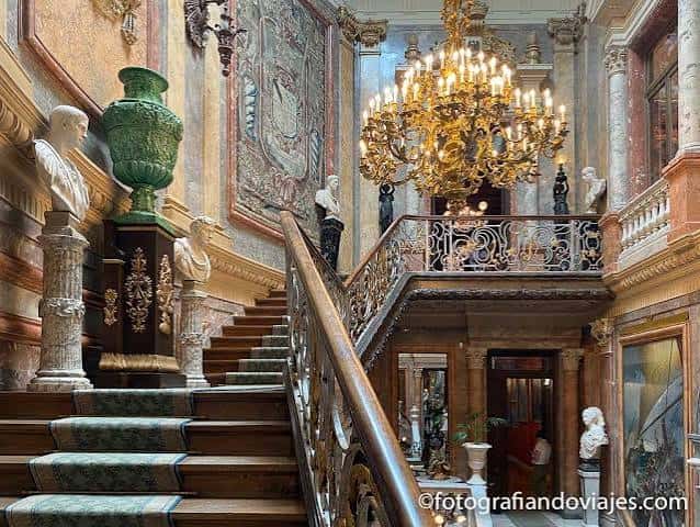 Escalera principal del Museo Cerralbo con barandilla de hierro forjado, bustos, tapices y un gran candelabro dorado colgante