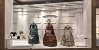 Exposición de vestidos históricos en vitrina con iluminación cálida