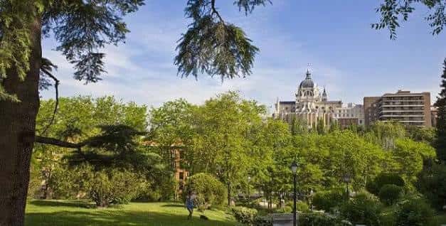 Vista desde los jardines con el Palacio de Cibeles dominando el horizonte entre árboles frondosos