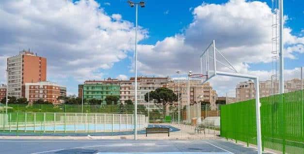 Cancha de baloncesto con valla verde y cielo parcialmente nublado