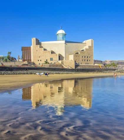 Reflejo del Auditorio Alfredo Kraus en el agua de la playa bajo un día soleado