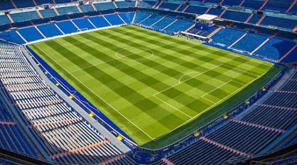 Vista panorámica del interior del estadio con gradas azules y campo de césped verde