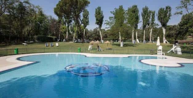Piscina exterior del Club de Campo Villa de Madrid con césped y árboles al fondo