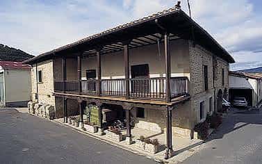 Fachada exterior del Centro Social de Manzanos, un edificio tradicional de piedra con balcón de madera