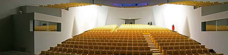 Interior del auditorio con butacas amarillas dispuestas en gradas y escenario iluminado