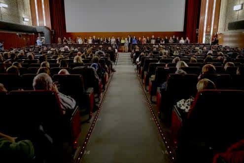 Interior del cine durante un evento con público sentado y personas en el escenario
