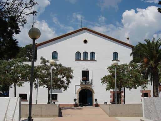 Fachada principal del edificio blanco con arcos y ventanas decorativas, rodeado de árboles