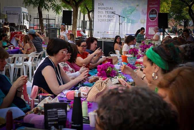 Evento comunitario en el Ágora con participantes sentados en mesas al aire libre