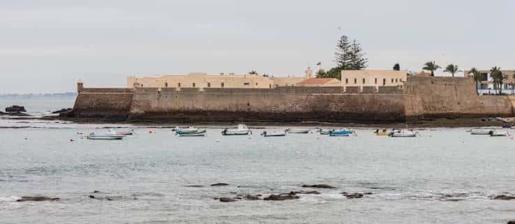 Panorámica del castillo desde el mar, mostrando sus murallas y barcas en primer plano
