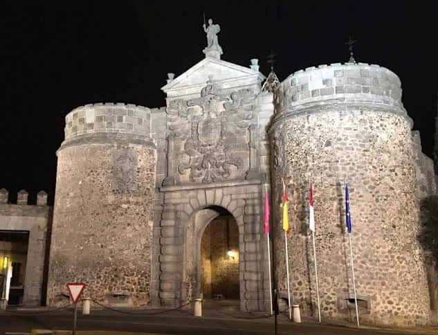 Puerta de Bisagra iluminada por la noche con banderas y estatua superior destacada