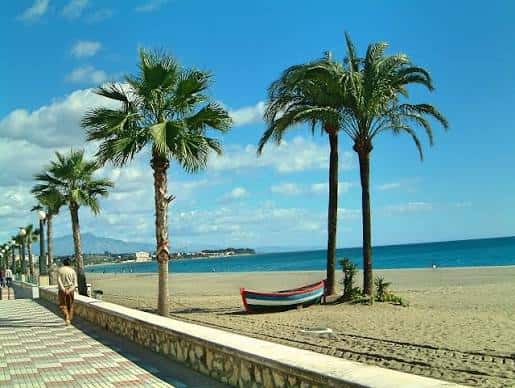 Paseo marítimo de La Rada con palmeras y una barca en la arena