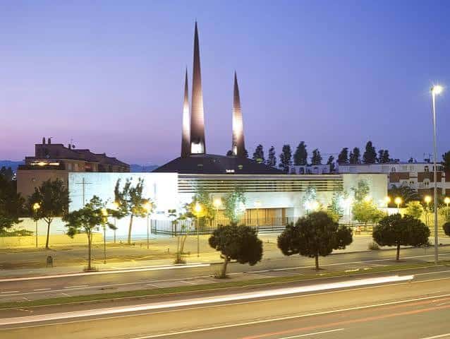 Vista nocturna de la fachada de la iglesia iluminada con las torres destacadas contra el cielo